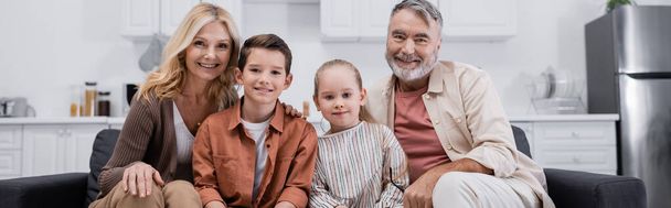 glückliche Kinder, die mit den Großeltern auf der Couch sitzen und in die Kamera lächeln, Banner - Foto, Bild
