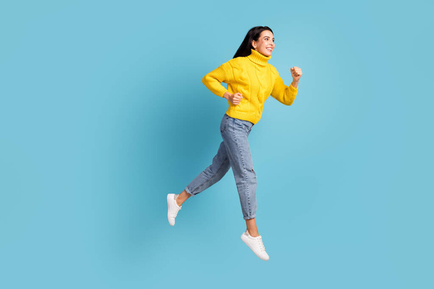 精力的な女性のジャンプランのプロフィール写真空のスペースは黄色のセータージーンズの靴を着用見て隔離された青の背景. - 写真・画像