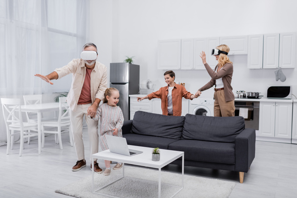 cheerful kids holding hands with grandparents gaming in vr headsets - Foto, afbeelding