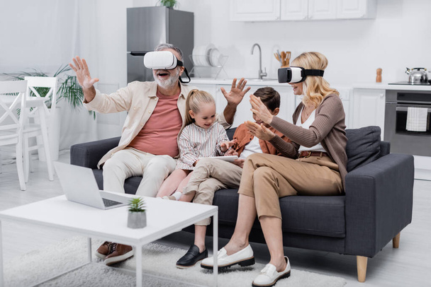 дети, использующие цифровой планшет вблизи возбужденных бабушки и дедушки игры в VR гарнитуры - Фото, изображение