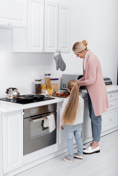 mulher de meia-idade feliz cozinhar na cozinha com a ajuda da neta pequena - Foto, Imagem