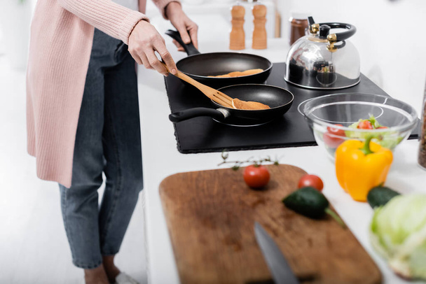 partial view of woman cooking pancakes near fresh vegetables on blurred foreground - Foto, Imagem