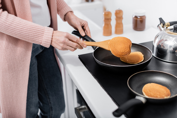 vista recortada de la mujer con tortitas de cocina espátula en sartenes - Foto, Imagen
