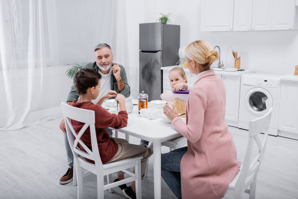 happy senior man looking at grandchildren and wife having breakfast in kitchen - Foto, imagen