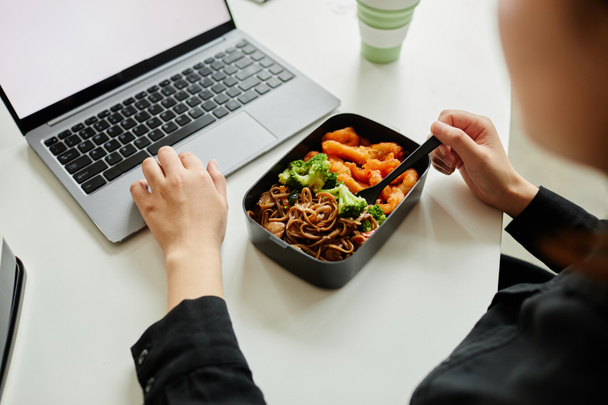 Primer plano de la mujer joven disfrutando de un almuerzo saludable con verduras mientras usa el ordenador portátil, espacio para copiar - Foto, imagen