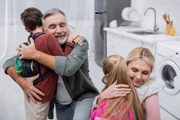 happy grandparents embracing grandchildren with backpacks at home - Fotografie, Obrázek