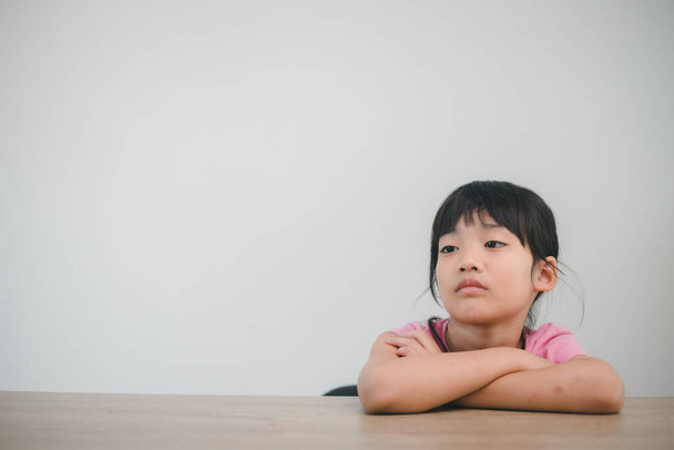 aziatische kind rust haar wangen op de vuisten met stemmig gezicht - Foto, afbeelding