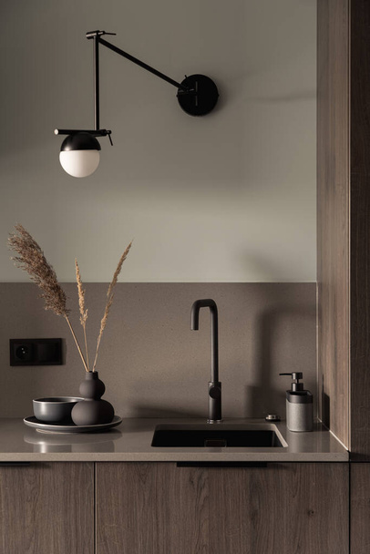 Close-up on stylish kitchen countertop with simple wooden furniture, black sink and tap and decorations - Foto, Imagen