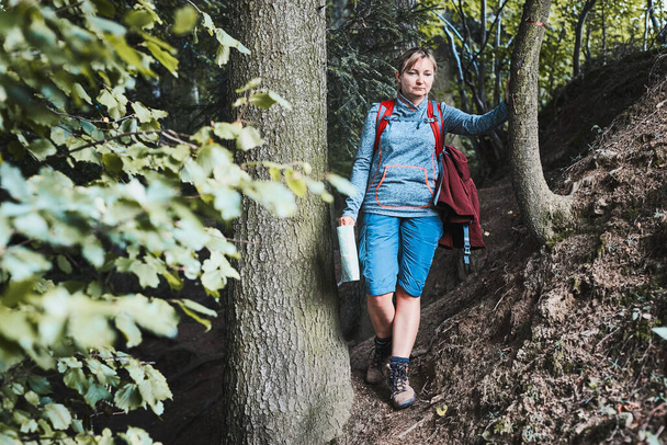 Active woman walking on forest path, actively spending summer vacation, carrying backpack, holding map - Фото, зображення