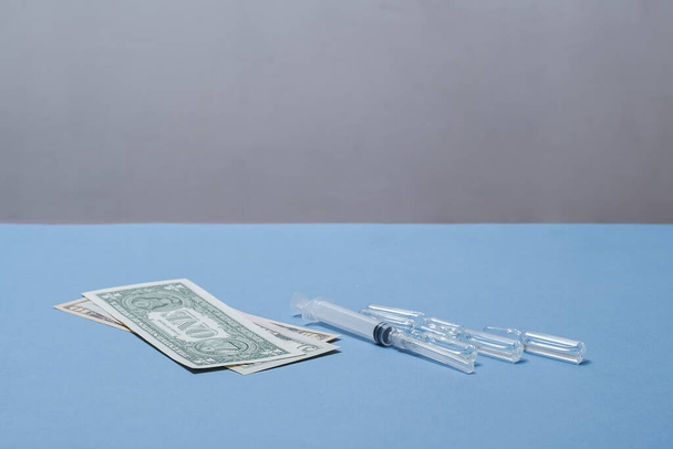 Money, a syringe and ampoules are on the table. - Фото, изображение