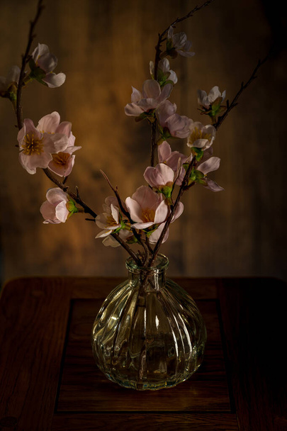 Bukiet wiosenno-różowe kwiaty w szklanym wazonie izolowane na tle drewna. - Zdjęcie, obraz