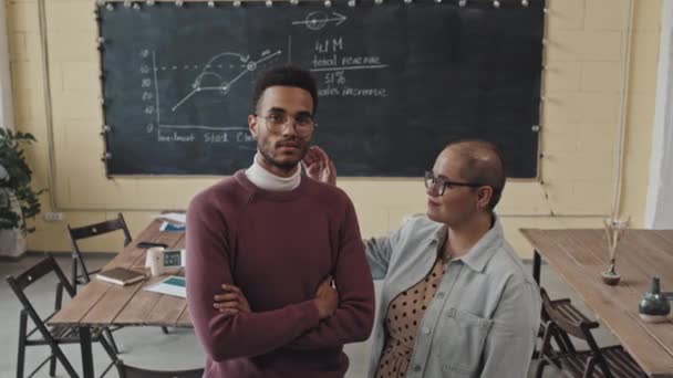 Portrait en grand angle d'un jeune homme Biracial et d'une femme aux cheveux courts portant des lunettes, debout dans une salle de classe moderne le jour, regardant et souriant à la caméra - Séquence, vidéo