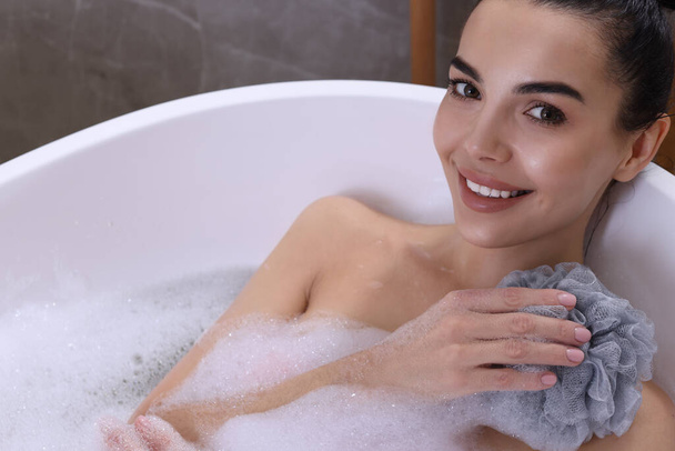 Woman taking bath with mesh pouf in tub, closeup - Fotografie, Obrázek