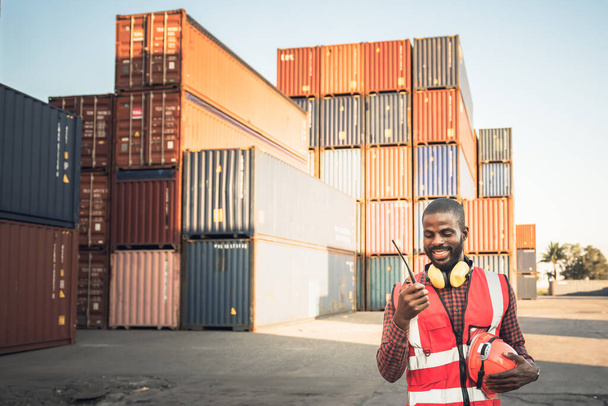 Afro-Amerikaanse arbeiders man, gebruik van een communicatie radio en werken in containers industrie, logistiek transport Import-Export Cargo, naar het bedrijfsleven scheepvaart en opslag haven terminal concept. - Foto, afbeelding
