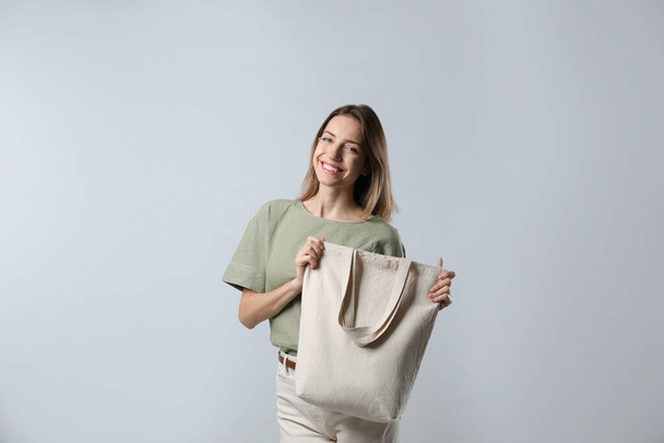 Happy young woman with blank eco friendly bag on light background - Foto, Bild