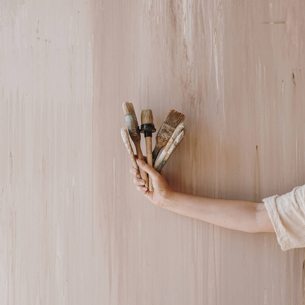 Woman's hand hold paintbrushes on neutral beige background. Minimalist art concept - Zdjęcie, obraz