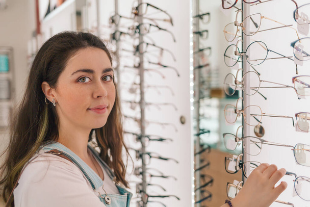 Здоров'я і зір. Молода красива жінка вибирає окуляри в оптичному магазині
. - Фото, зображення