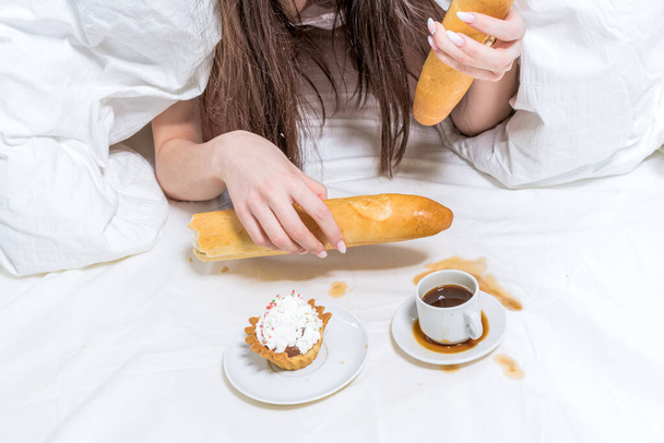 Pastel on which the girl lies, next to her a cupcake, a baguette in her hand and spilled on a cup of coffee. Drink stain. Dirt. - Foto, Imagen