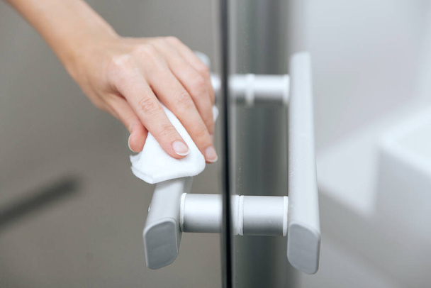 Cleaning glass door handles with an antiseptic wet wipe. Woman hand using towel for cleaning home room door link. Sanitize surfaces prevention in hospital and public spaces against corona virus - Foto, Bild