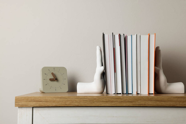Beautiful hand shaped bookends with books and clock on table near light wall - Foto, Bild