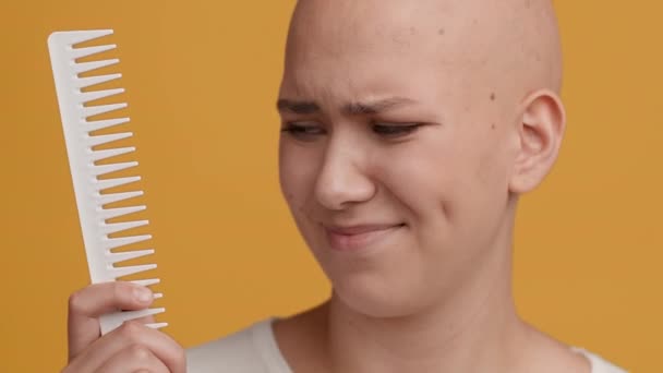 Glatzköpfige Dame hält Kamm und schüttelt den Kopf über gelben Hintergrund - Filmmaterial, Video