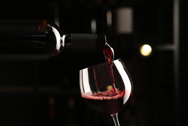 Pouring red wine from bottle into glass on blurred background, closeup - Fotoğraf, Görsel