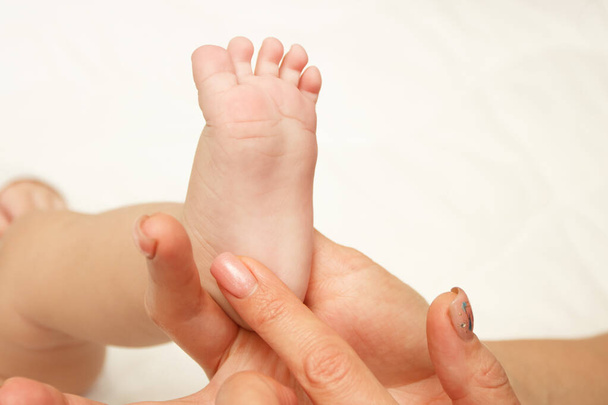 Hands of woman holds baby foot, soft focus background - Foto, Imagen