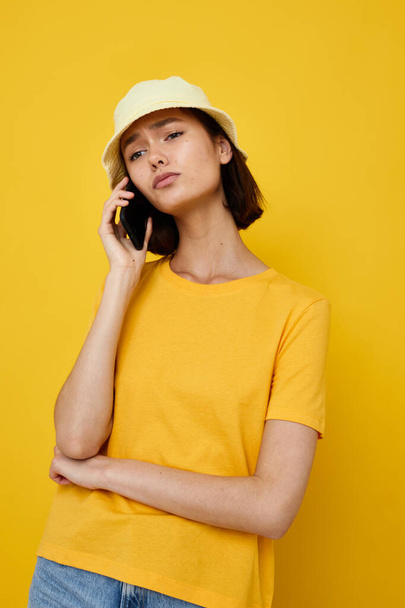 young woman yellow t-shirt and Hat summer style with phone yellow background - Foto, afbeelding