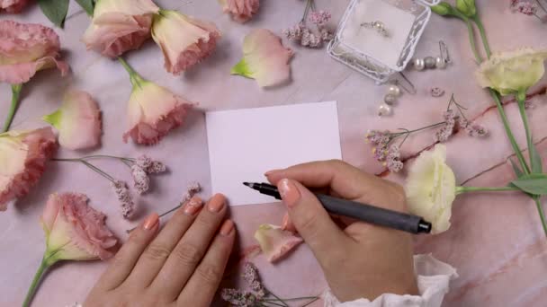 Ruce psaní LOVE na kartičku v blízkosti růžových květin zavřít na mramorovém stole - Záběry, video
