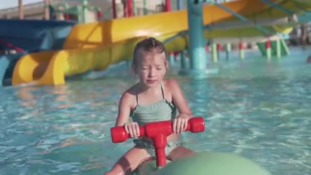 A little girl rides a swing in the pool at the water park in the summer - Materiaali, video