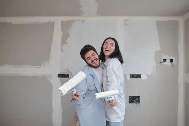 Giovane coppia che canta con rulli di vernice e ride mentre dipinge pareti. - Foto, immagini