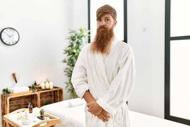 Rudy mężczyzna z długą brodą w szlafroku w spa wellness z poważnym wyrazem twarzy. proste i naturalne patrzenie w kamerę.  - Zdjęcie, obraz