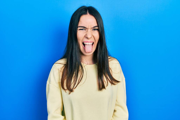Young brunette woman wearing casual sweatshirt sticking tongue out happy with funny expression. emotion concept.  - Foto, afbeelding