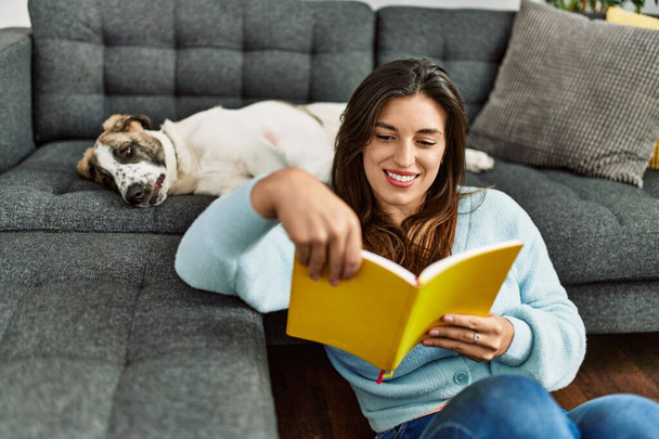 Νεαρή γυναίκα διαβάζει βιβλίο κάθεται με το σκυλί στο σπίτι - Φωτογραφία, εικόνα