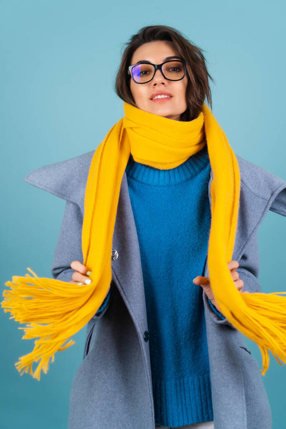Portrait printanier d'automne d'une femme en pull tricoté bleu, lunettes, écharpe jaune vif et manteau gris, posant à la mode, en prévision du printemps - Photo, image