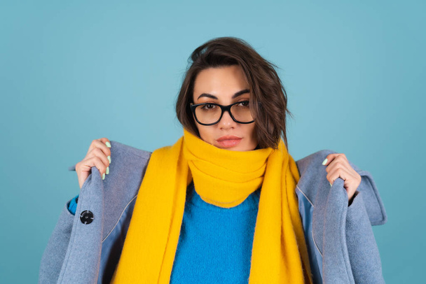 Spring autumn portrait of a woman in a blue knitted sweater, glasses, a yellow bright scarf and a gray coat, posing fashionably, in anticipation of spring - Photo, Image