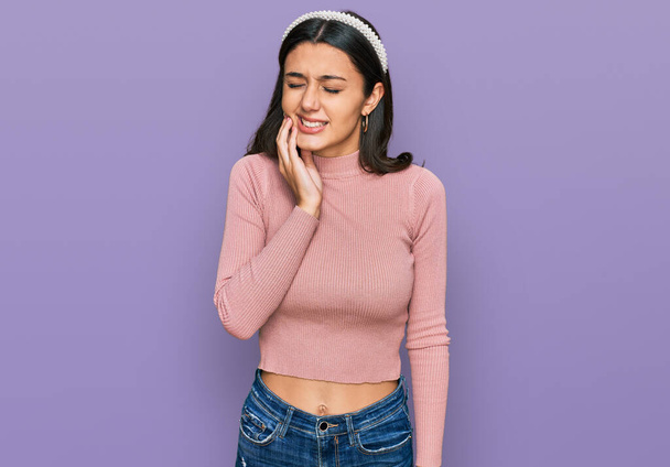 Νεαρή ισπανόφωνη κοπέλα που φοράει καθημερινά ρούχα αγγίζοντας το στόμα με το χέρι με επώδυνη έκφραση λόγω πονόδοντος ή οδοντικής πάθησης στα δόντια. οδοντίατρος  - Φωτογραφία, εικόνα