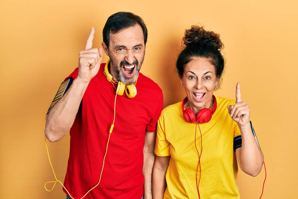 Middle age couple of hispanic woman and man wearing sportswear and arm band pointing finger up with successful idea. exited and happy. number one.  - Фото, изображение