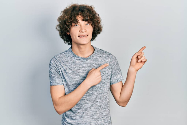 Handsome young man wearing casual grey t shirt smiling and looking at the camera pointing with two hands and fingers to the side.  - Photo, Image