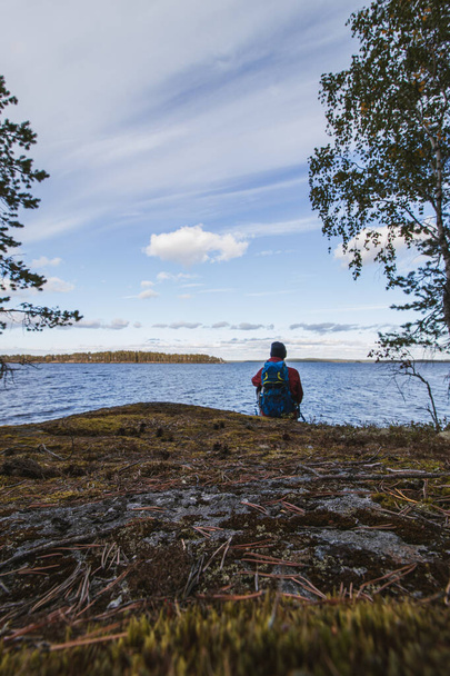 turista v bundě a s batohem, stojící na skále a sledující Jatkonjarviho jezero při západu slunce v národním parku Koli ve východním Finsku. Muž ve věku 24 let ve sportovním oblečení. Aktivní životní styl. - Fotografie, Obrázek