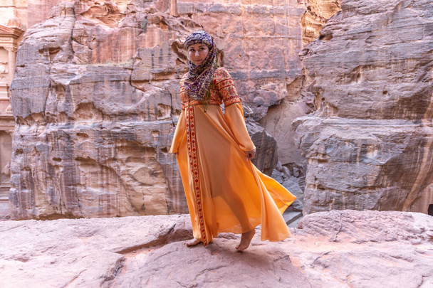 Žena oblečená do tradičních šatů a šátek, které zůstávají na vrcholu skály na pozadí je Petra Palace - Fotografie, Obrázek