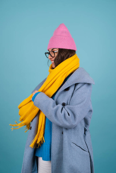 Mavi örgü süveter, gözlük, sarı parlak bir eşarp ve gri bir palto giyen pembe şapkalı neşeli poz veren bir kadının bahar sonbahar portresi. - Fotoğraf, Görsel