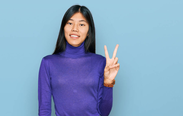 Gyönyörű fiatal ázsiai nő alkalmi ruhát visel mosolygós nézi a kamera mutatja ujjak csinál győzelem jele. Második..  - Fotó, kép