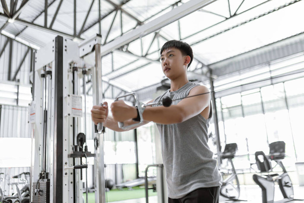 exercise concept The male working out club subscriber standing and giving focus on doing curl pulling the spring rope toward himself together with his both hands. - 写真・画像