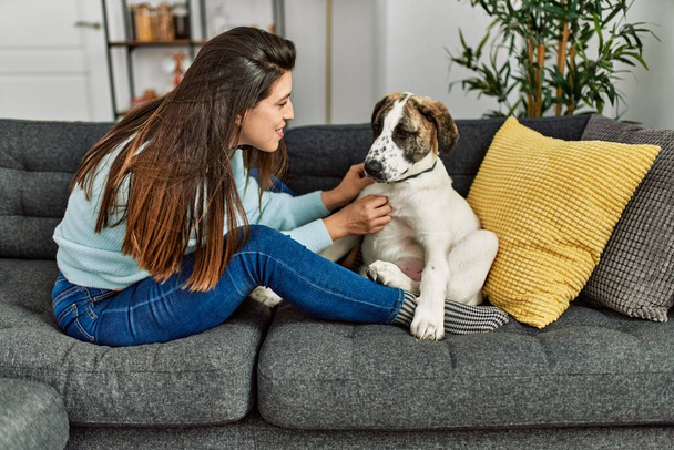 Young woman hugging dog sitting on sofa at home - Фото, изображение