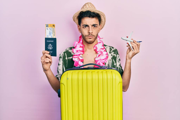 若いヒスパニック系の男性は夏のスタイルとハワイレイを保持パスポートと飛行機のおもちゃ懐疑的かつ神経を着て、問題のために動揺を眉をひそめて。否定的な人.  - 写真・画像
