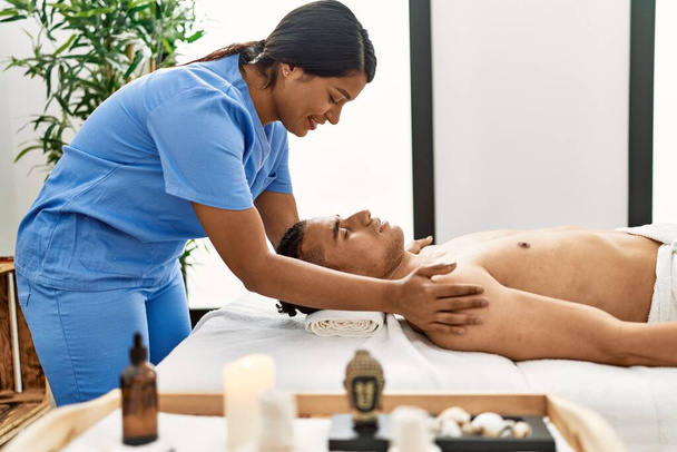Joven masaje latino terapeuta mujer dando un tratamiento relajante en los hombros del hombre en el centro de belleza. - Foto, imagen