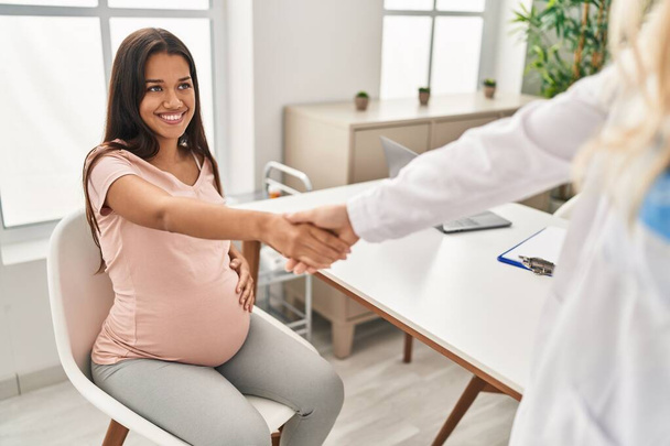Young latin woman pregnant and doctor shake hands at clinic - Fotó, kép