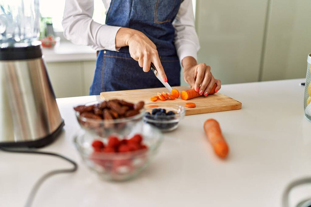 Νεαρή ξανθιά γυναίκα κόβει καρότο στην κουζίνα - Φωτογραφία, εικόνα