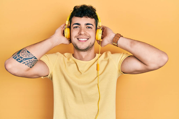 若いヒスパニック系の男性の音楽をヘッドフォンを使用して顔に幸せとクールな笑顔で笑顔を聞いて。歯を見せて.  - 写真・画像
